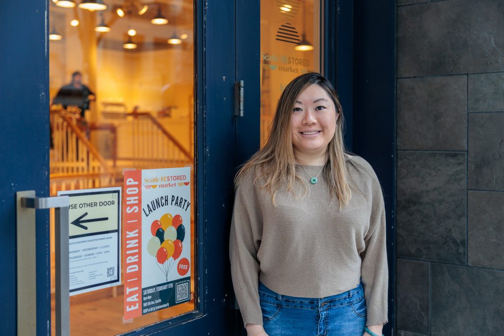 Christina Chan of Dyme Designs poses in front of the storefront at the Seattle Restored Collective Marketplace.