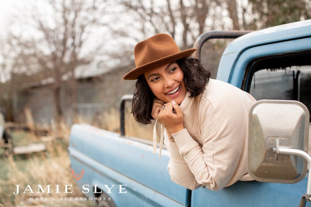 A person leans out of a truck posing with a Jamie Slye hat.