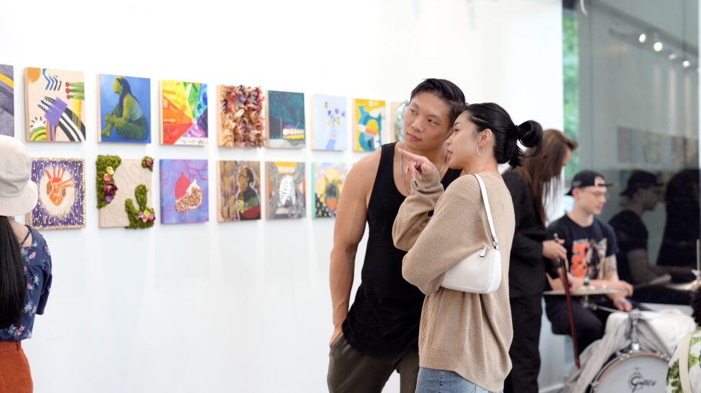 Unwritten Group show opening featuring a young eastern asian couple looking at a wall of colorful artworks